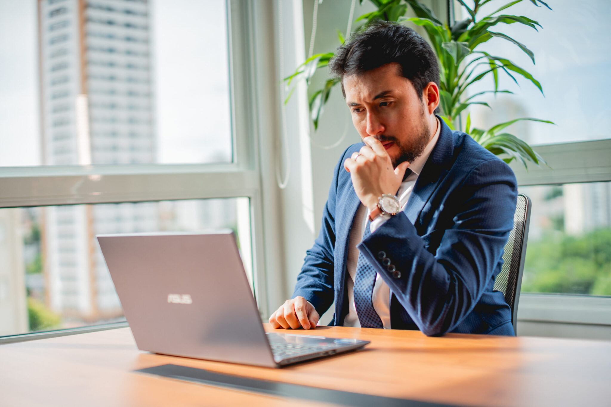 advogado de terno sentado olhando para seu notebook apoiado em uma mesa de madeira